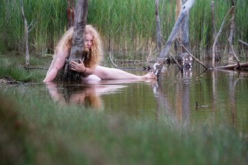 sexy nude lying mature red-haired woman as nymph mermaid in the water of Restloch 1332 behind dead tree trunks in Weißwasser, Oberlausitz,