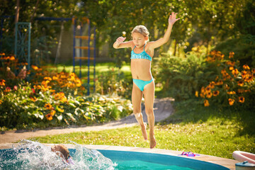 Cute little girl jumping into the swimming pool during summer