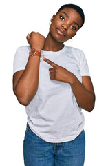 Young african american woman wearing casual white t shirt in hurry pointing to watch time, impatience, looking at the camera with relaxed expression