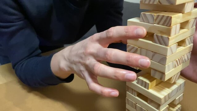 A lively group of friends is engrossed in a fun game of Jenga, stacking wooden blocks – a close-up captures hands pulling out a block. the concept of board games and social gatherings