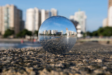 Glass ball with focus reflecting the buildings on the beach in the city of Santos, Brazil. Blurred background in a late afternoon with blue sky.