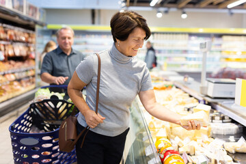 Elderly woman choose cheese in supermarket