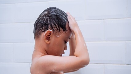 Asian young boy is standing in the shower with his hair wet