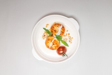 Top view fried cheesecakes with sour cream and cherry tomatoes on a white plate