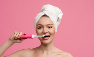 attractive woman in bath towel posing on pink background after shower with tooth brush