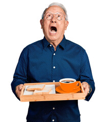 Senior man with grey hair holding tray with lunch and coffee angry and mad screaming frustrated and...