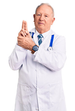 Senior handsome grey-haired man wearing doctor coat and stethoscope holding symbolic gun with hand gesture, playing killing shooting weapons, angry face