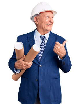 Senior handsome grey-haired man wearing architect hardhat holding blueprints pointing thumb up to the side smiling happy with open mouth