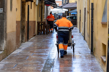 Men with brooms and cleaning carts walk the streets, removing waste and keeping the city clean. - obrazy, fototapety, plakaty