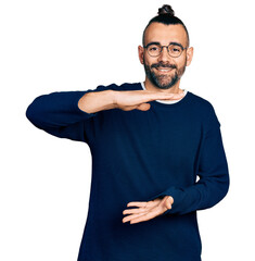 Hispanic man with ponytail wearing casual sweater and glasses gesturing with hands showing big and...