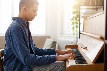 Young man playing piano in bright room © Prostock-studio