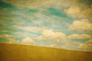 Vintage background of green field and blue cloudy sky .