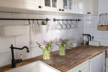 Beautiful views light white kitchen with bouquets of flowers on wooden countertop, highlighting...
