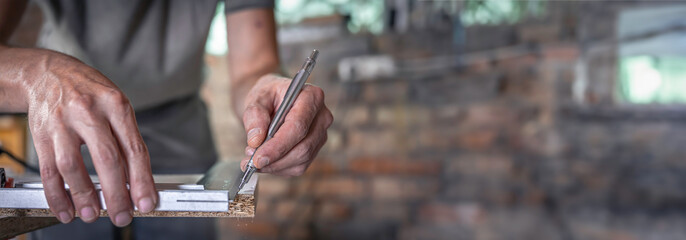 Carpenter holding ruler and pencil while making marks on the wood. - obrazy, fototapety, plakaty