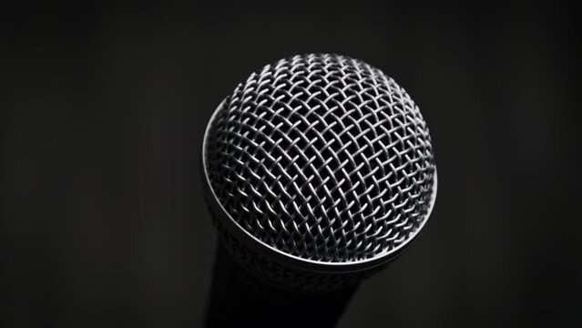Dynamic handheld microphone rotates on a black background. Mic on a stand slowly turning. Close-up chrome grid of mic surface. Concept recording studio, voice, podcast, karaoke, audiobook. Copy space