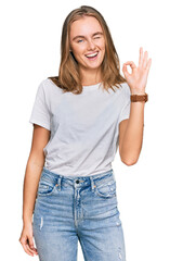 Beautiful young blonde woman wearing casual white t shirt smiling positive doing ok sign with hand and fingers. successful expression.
