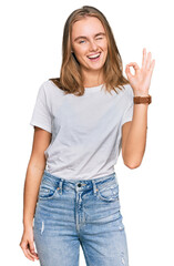 Fototapeta premium Beautiful young blonde woman wearing casual white t shirt smiling positive doing ok sign with hand and fingers. successful expression.