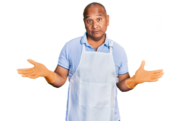 Hispanic middle age man wearing cleaner apron and gloves clueless and confused expression with arms and hands raised. doubt concept.