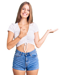 Young beautiful blonde woman wearing casual white tshirt showing palm hand and doing ok gesture with thumbs up, smiling happy and cheerful