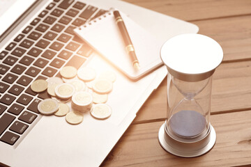Office supplies, coins, and hourglass placed on a laptop