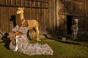 Beautiful young happy woman with cute alpacas on a summer day at the alpaca ranch. Pretty Girl with...
