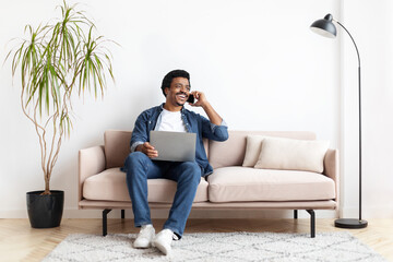 Smiling Black Man Talking On Phone And Using Laptop At Home