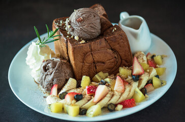 Plate of french toast topped with chocolate ice cream, mixed berries, banana and maple syrup and  on dark background..