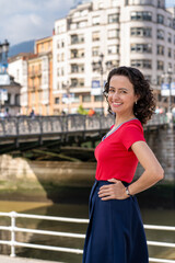 Enigmatic Elegance: Woman in Red Top and Blue Skirt Standing by Bridge in Bilbao.