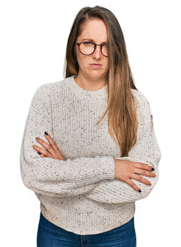Young blonde woman wearing casual sweater and glasses skeptic and nervous, disapproving expression on face with crossed arms. negative person.