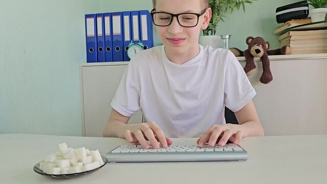 Teenager guy eats sugar while working at the computer at home. Sweet addiction, uncontrolled consumption of sugar in teenagers and children