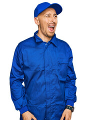 Bald man with beard wearing builder jumpsuit uniform angry and mad screaming frustrated and furious, shouting with anger. rage and aggressive concept.