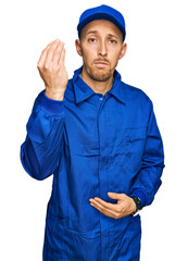 Bald man with beard wearing builder jumpsuit uniform doing italian gesture with hand and fingers confident expression