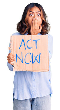 Young beautiful mixed race woman holding act now banner covering mouth with hand, shocked and afraid for mistake. surprised expression