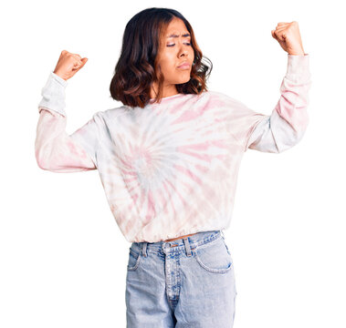 Young beautiful mixed race woman wearing casual tie dye sweatshirt showing arms muscles smiling proud. fitness concept.