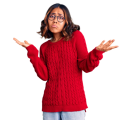 Young beautiful mixed race woman wearing red sweater and glasses clueless and confused expression with arms and hands raised. doubt concept.