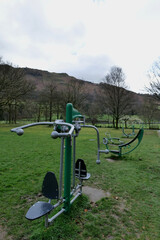 Fototapeta premium Exercise machines lined up in a public park with hills and trees in the background