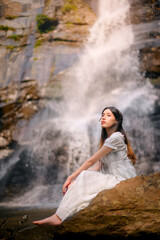 beautiful asian woman wearing white dress standing in front of waterfall in natural park