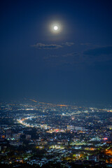 Naklejka premium full moon over Chiang mai city at night, aerial view City night from the view point on top of mountain 