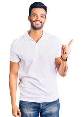 Young handsome hispanic man wearing casual clothes with a big smile on face, pointing with hand finger to the side looking at the camera.