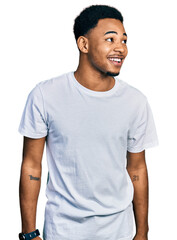 Young african american man wearing casual white t shirt looking away to side with smile on face, natural expression. laughing confident.