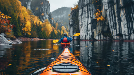rear view of a man on a kayak floating on a serene mountain lake surrounded by steep cliffs and forest in autumn