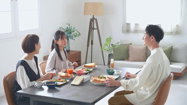 A family of an Asian girl and her parents sit around the dining table and enjoy a meal.
