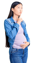 Young beautiful chinese woman pregnant expecting baby thinking concentrated about doubt with finger...