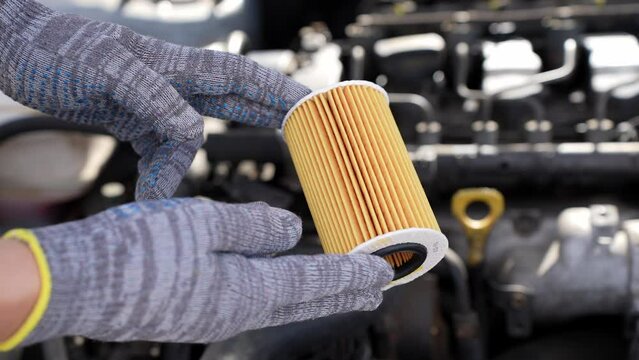 Auto mechanic holds an oil filter for diesel cars in his hands against background of engine compartment, close-up. Concept of auto parts replacement, oil change and car oil filter, car maintenance.