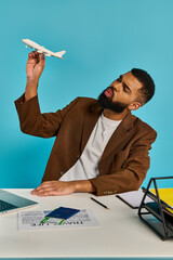 A man sits at a desk, focused on a laptop screen while a model airplane sits beside him, showcasing his passion for aviation.