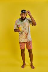 Fototapeta premium A stylish man in a vibrant tie dye shirt is holding a refreshing drink in his hand, exuding a carefree and relaxed vibe.