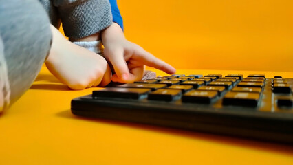 A small child counts on a calculator on a yellow background. Kid fingers press buttons and calculate studying math at home. Child makes arithmetic calculations with a calculator - obrazy, fototapety, plakaty