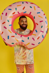 A man playfully hides his face behind a massive donut, showcasing his whimsical and humorous side...
