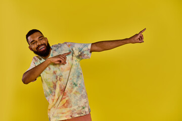 A man wearing a vibrant tie dye shirt points animatedly at something out of frame, his colorful...