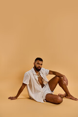 A man sits on the ground with his legs crossed, deep in thought, his gaze focused ahead as if...